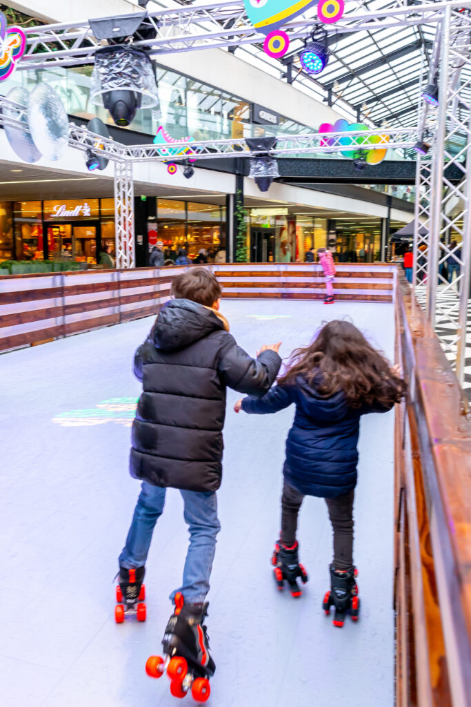 Deux enfants patinant main dans la main sous la verrière d'une galerie